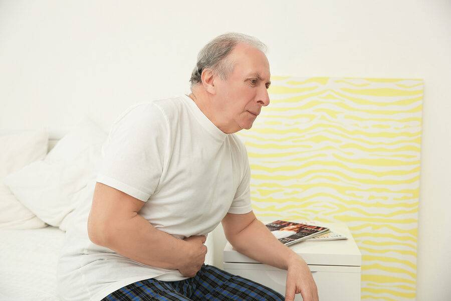 senior-man-suffering-from-abdominal-pain-while-sitting-on-bed-at