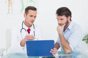 male-doctor-discussing-reports-with-patient-at-desk-in-medical-office