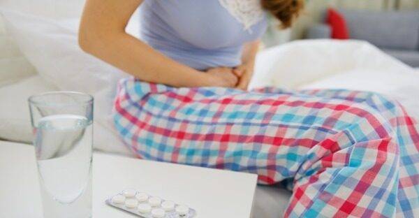 glass-of-water-and-pills-on-table-and-woman-with-abdominal-ache-in-background